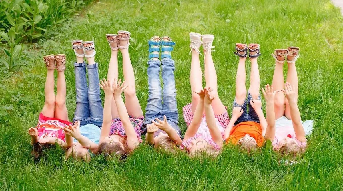 a group of children playing and running in the park on a green gozon